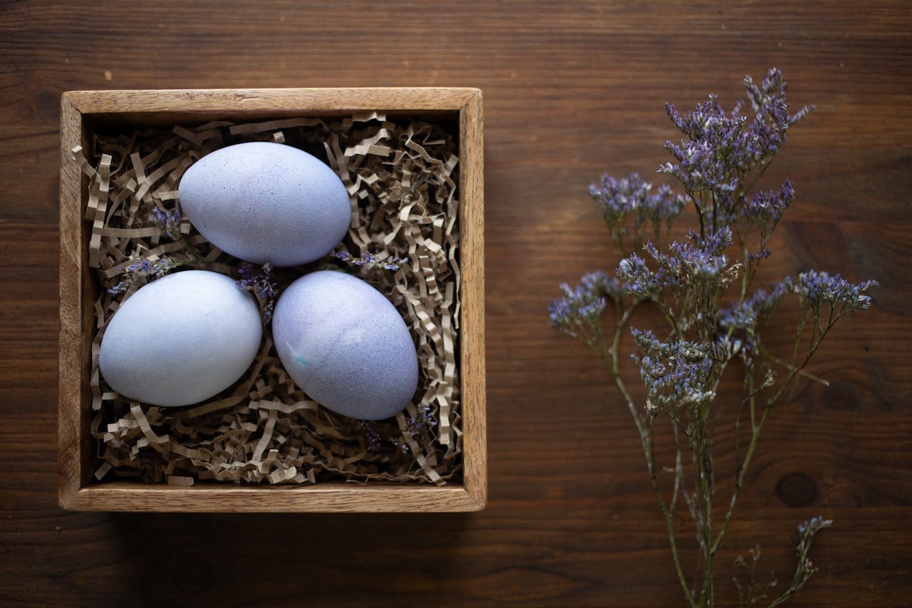 Three decorative purple Easter eggs in a wooden box with dried lavenders on a wooden table.